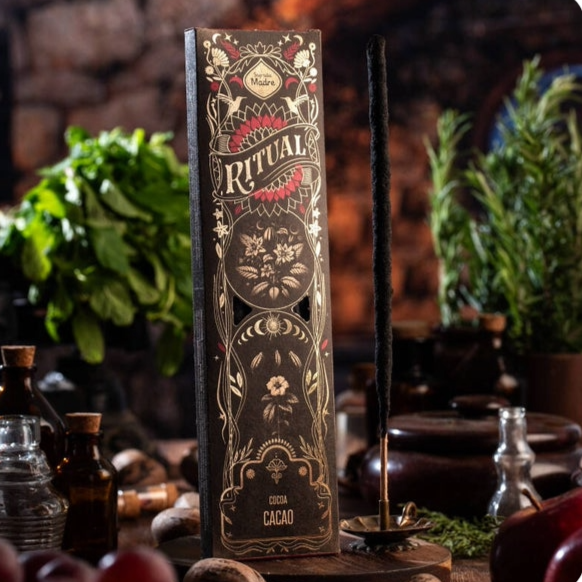 Een doosje Sagrada Madre Rituals wierook met cacaogeur, gepresenteerd op een rustieke houten achtergrond. Het doosje bevat 6 wierookstokjes, elk met een brandtijd van 60 minuten, gemaakt van essentiële olie, houtskool, natuurlijk bindmiddel en zout. Perfect voor spirituele rituelen en meditatie.