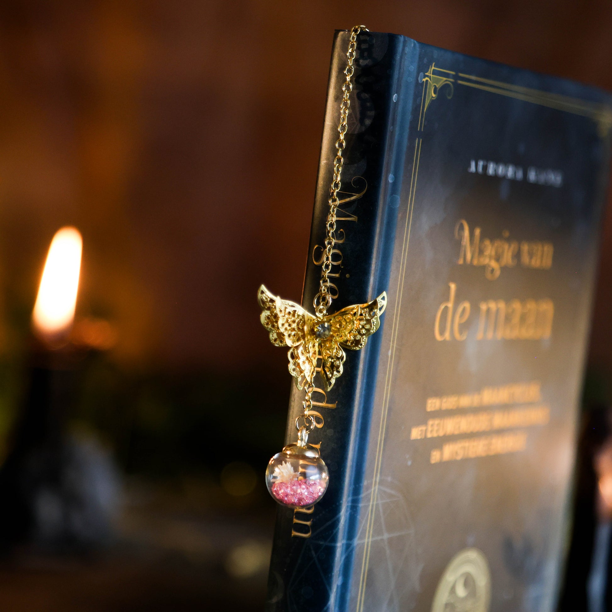 Detailfoto van gouden boekenlegger met vlinder en kristalbol met paarse steentjes op donkere achtergrond hangend aan een boek