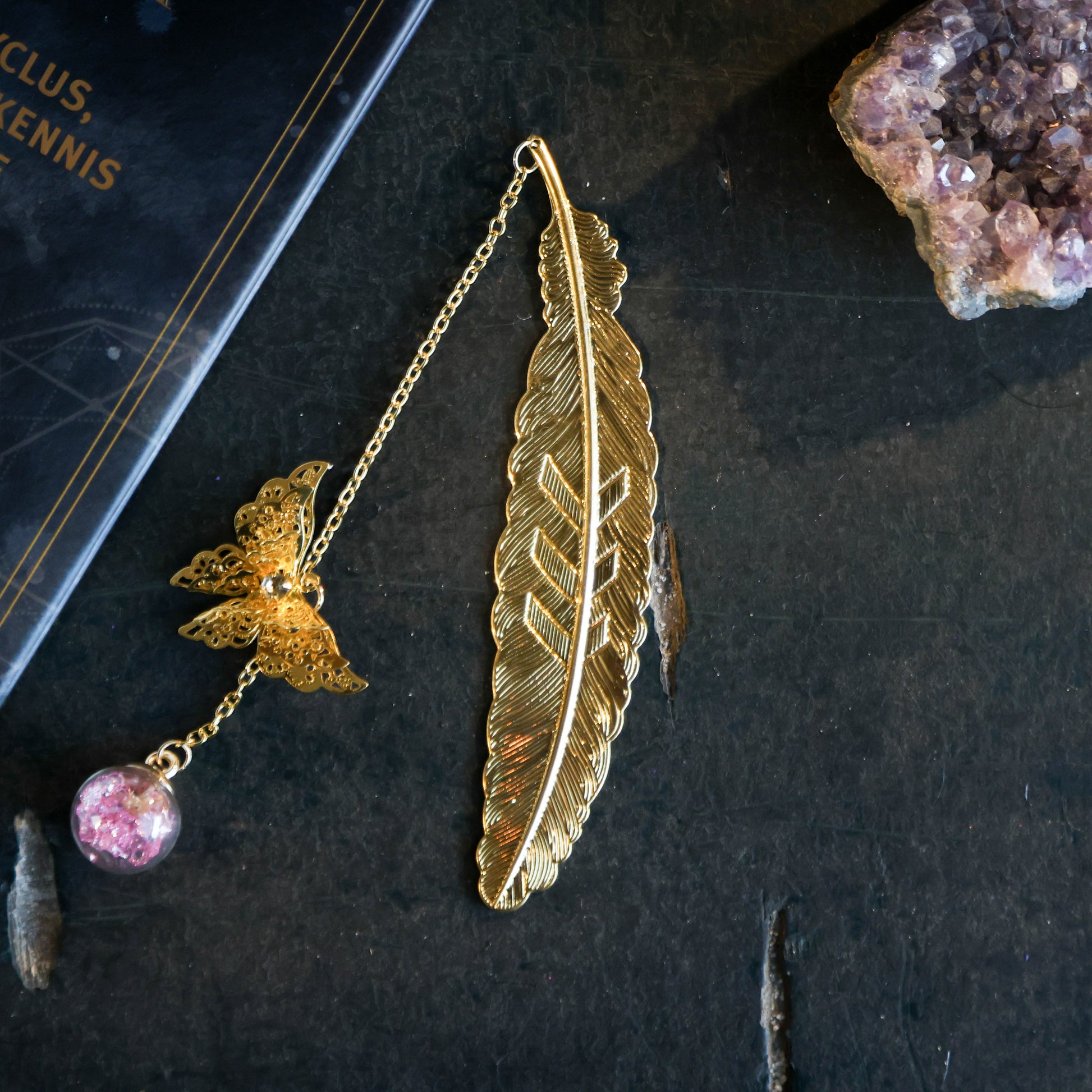 Gouden boekenlegger met veer, vlinder en glazen bol gevuld met roze kristalsteentjes – lengte 24 cm, spirituele uitstraling.