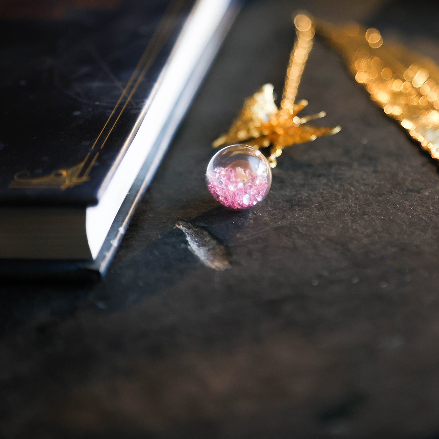 Detailfoto van gouden boekenlegger met vlinder en kristalbol met paarse steentjes op donkere achtergrond naast boek.