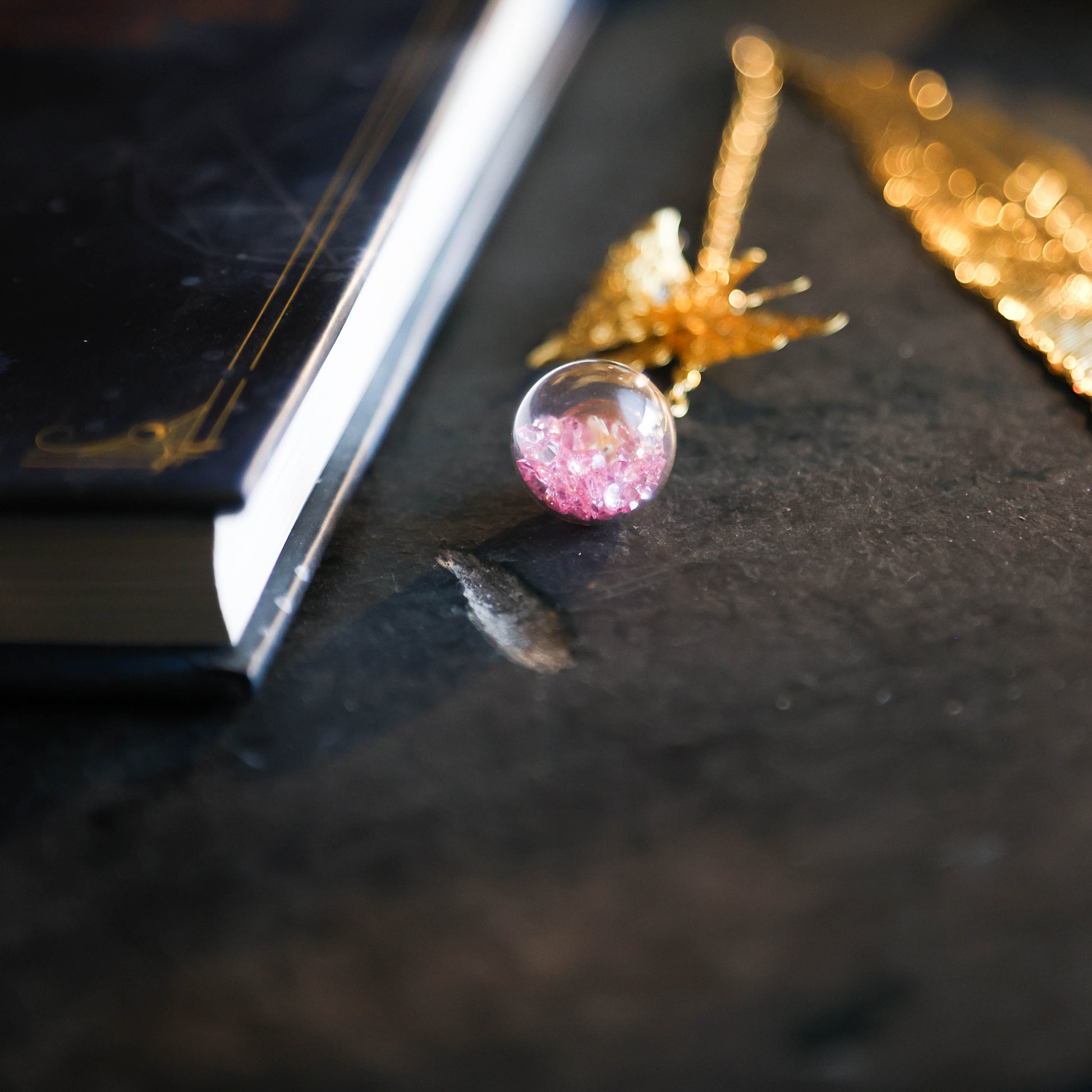 Detailfoto van gouden boekenlegger met vlinder en kristalbol met paarse steentjes op donkere achtergrond naast boek.